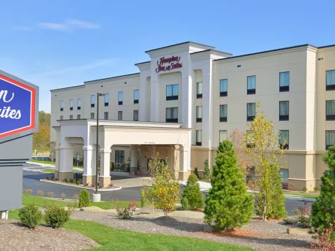 The image shows the exterior of a Hampton Inn & Suites hotel by Hilton with green landscaping and a prominent sign in the foreground.