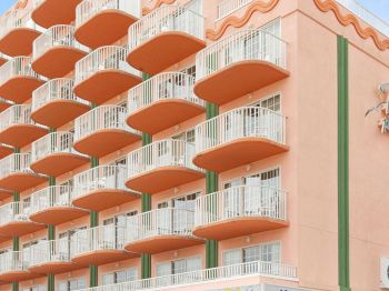 The image shows a multi-story hotel building with numerous balconies and a sign that reads 